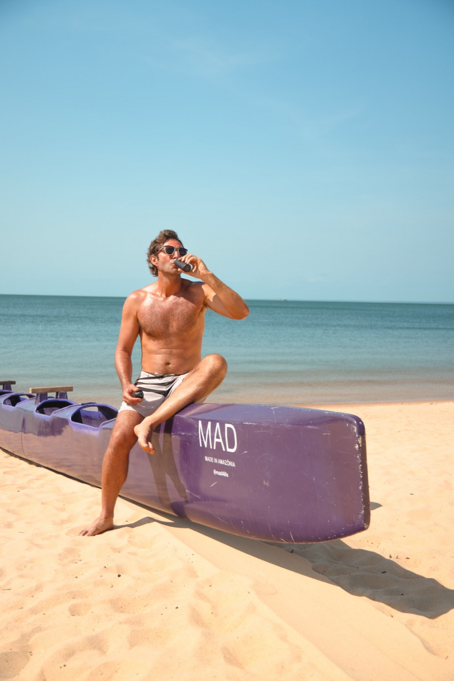 Homem tomando o Shot MAD sentado em uma canoa na praia